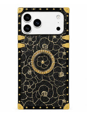 A protective phone case with a black textured background, gold floral patterns, and gold corner accents, shown on a white phone against a plain white background.