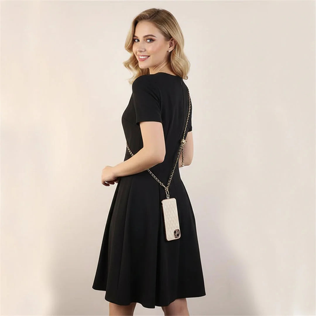 Woman wearing a black dress with a white handbag on a plain background