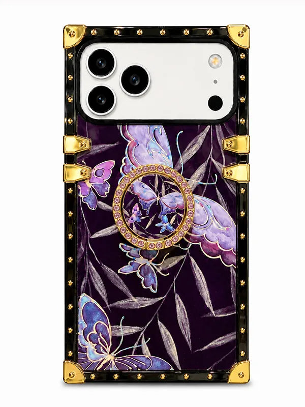 A protective phone case with a luxury trunk design, featuring a dark purple background decorated with purple and blue butterflies, gold metallic corner protectors, and a central gold ring stand embellished with small clear rhinestones.