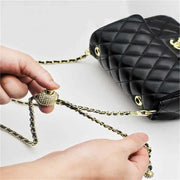 Black quilted handbag with gold chain and clasp on a light gray background