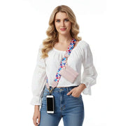 Woman wearing a white blouse, blue jeans, and a pink crossbody phone strap with a colorful strap.