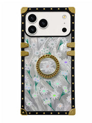 A protective phone case with a clear back decorated with a white daisy and green stem pattern over a silver glitter background. It features a gold circular pop socket in the center, a black border, and gold metal corner guards and rivets.