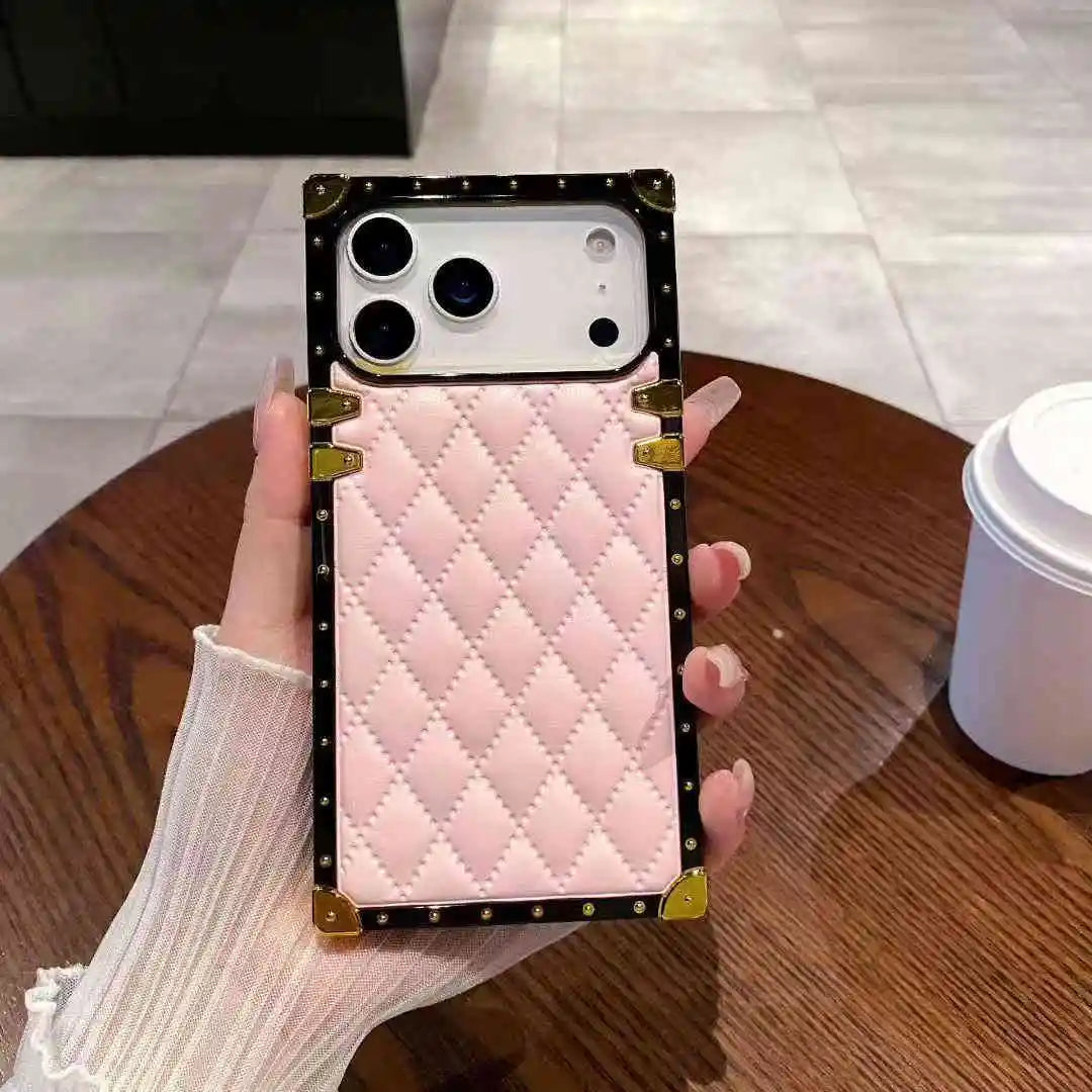 Pink quilted phone case with gold accents held by a hand on a wooden table.