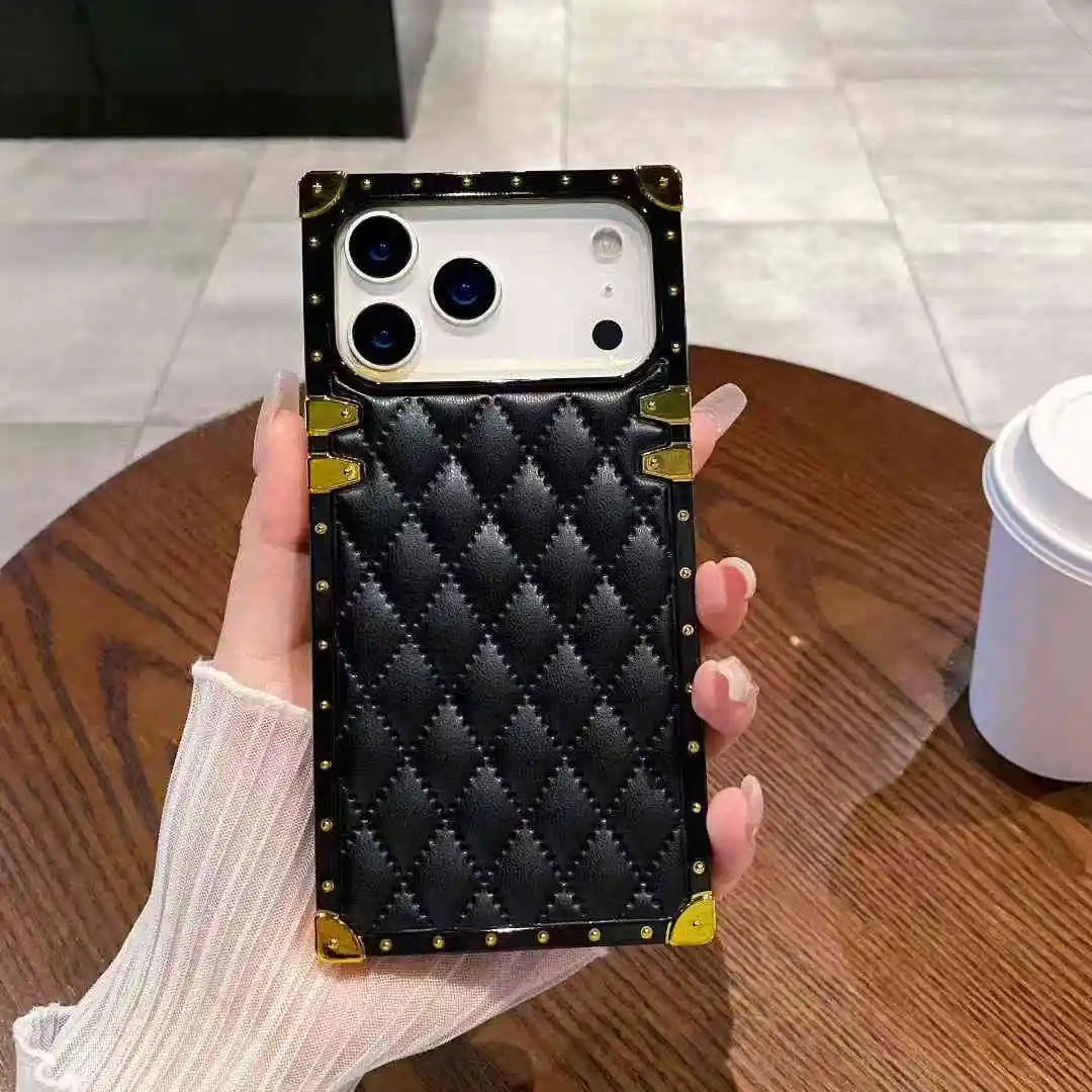 Black quilted phone case with gold accents held by a hand on a wooden table.
