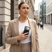 Woman in a beige blazer holding a phone in luxury trunk case on a city street