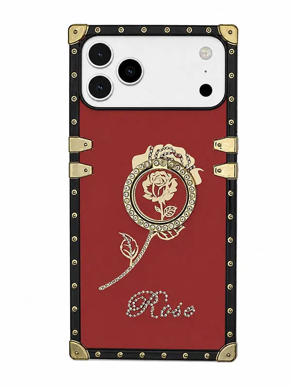 A red phone case with a vintage suitcase-inspired design, featuring gold-tone corner protectors, rivets, and a central rose medallion with the name 'Rise' in rhinestone script at the bottom.