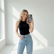 Woman taking a mirror selfie wearing a black top and light blue jeans in a bright room.