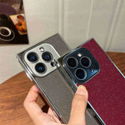 Two smartphones with reflective cases being held by a hand on a wooden surface.