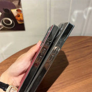 Person holding a smartphone with a reflective case on a wooden surface.