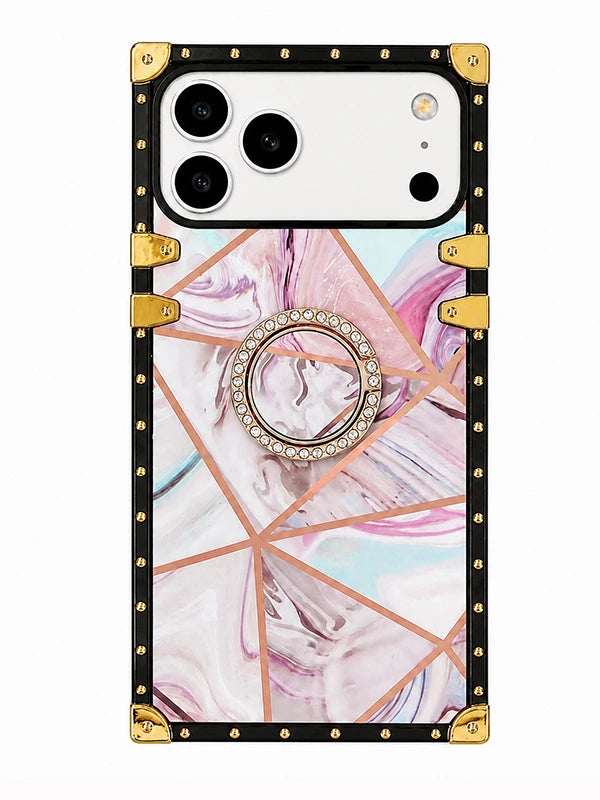 A protective phone case with a black border, gold corner protectors and rivets, a geometric rose gold line pattern, and a pink and white marble swirled center. It features a built-in ring holder in the middle adorned with clear rhinestones.