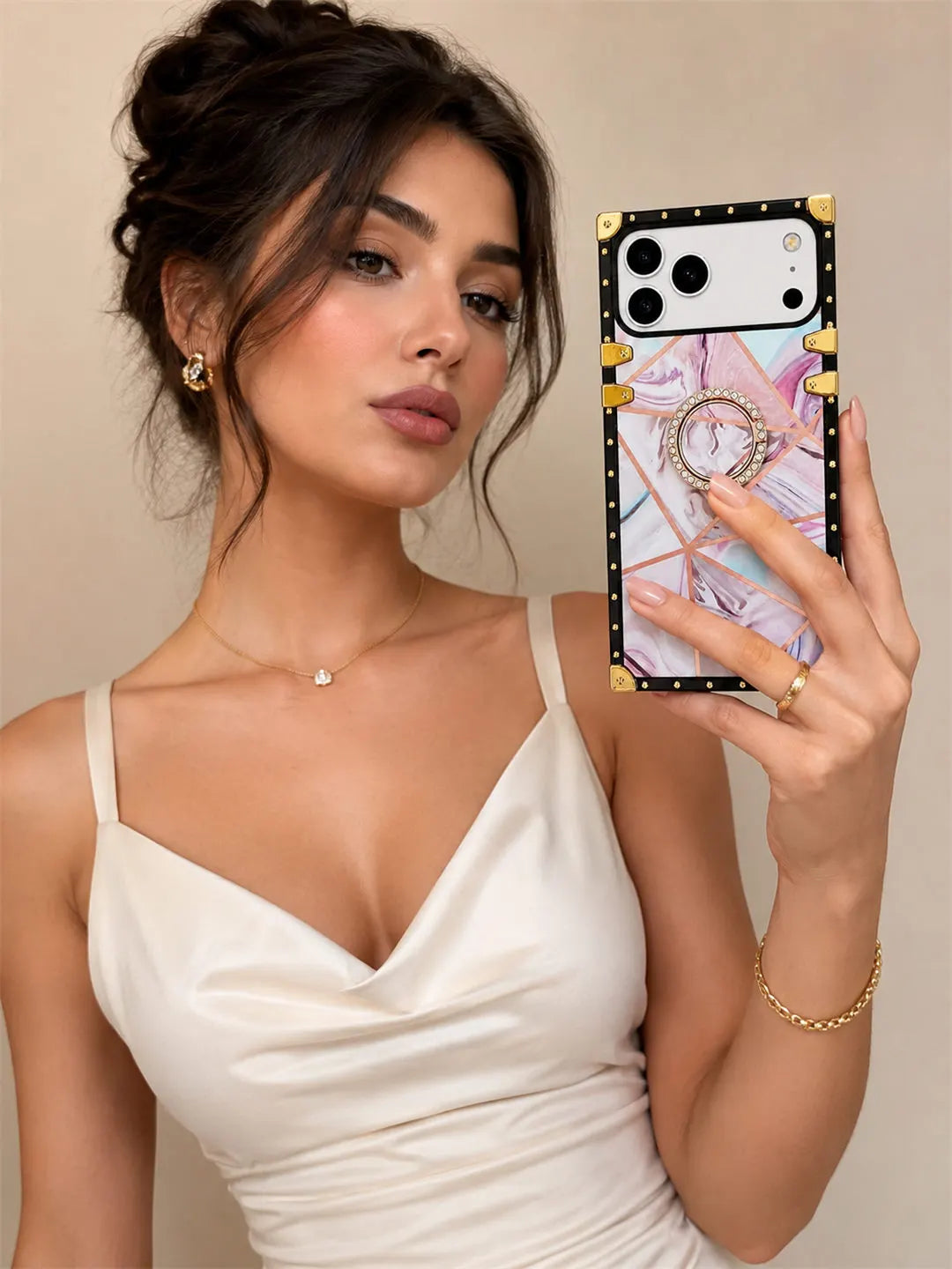 A woman in a white camisole takes a mirror selfie showing off a phone case. The phone case features a black border with gold studs, a colorful marble-patterned back, and a built-in ring stand.