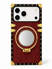 A luxury-style phone case with a red rhinestone-embossed body, black trim, gold corner protectors and hardware, and a circular mirror integrated into the center ring stand, shown on a white background.