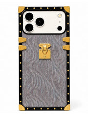 A luxury-style phone case designed to look like a vintage trunk, featuring a textured gray wavy pattern, black trim, gold-tone studs, corner protectors, and a central gold clasp, shown on a white background.