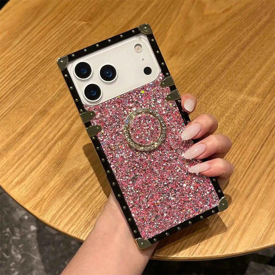 Phone case with pink glittery design and ring holder held by a hand on a wooden surface