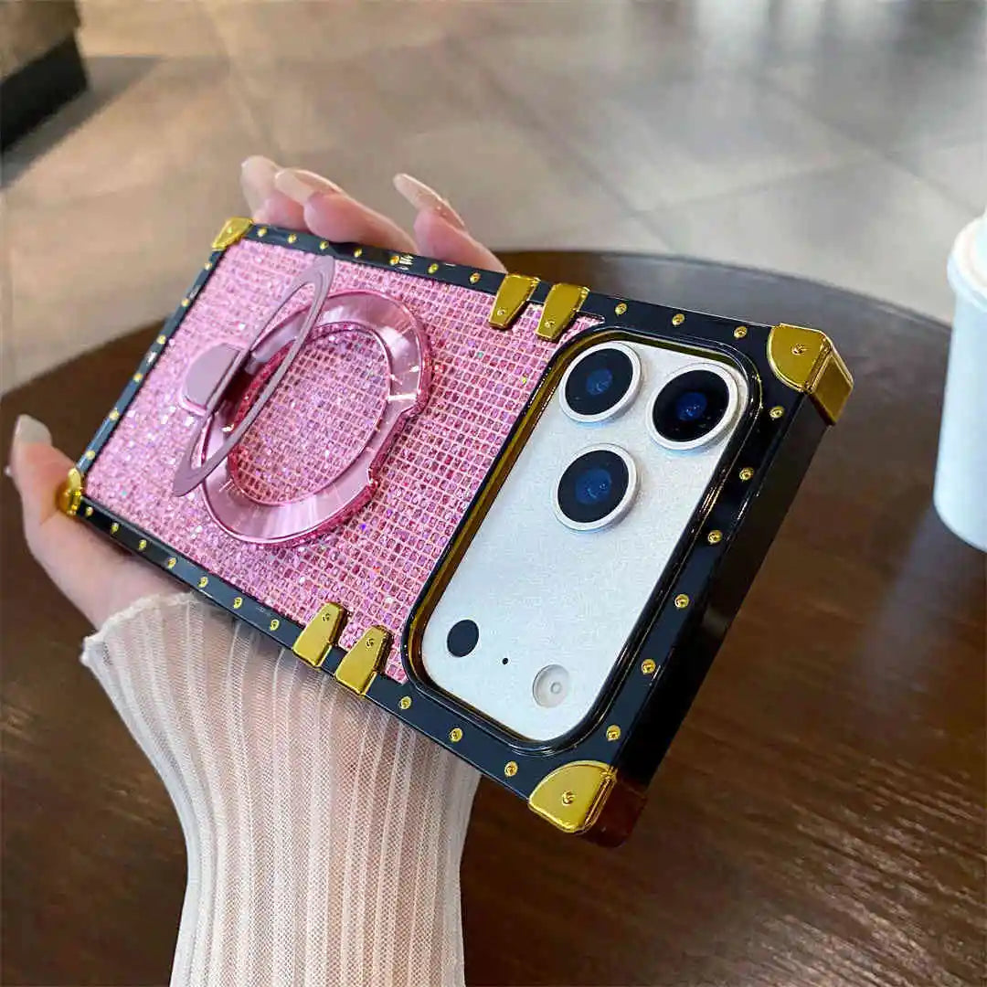 Phone case with pink glittery design and gold accents held by a hand on a wooden surface.