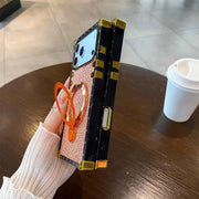 Person holding a phone with a decorative case on a wooden table with a coffee cup in the background.