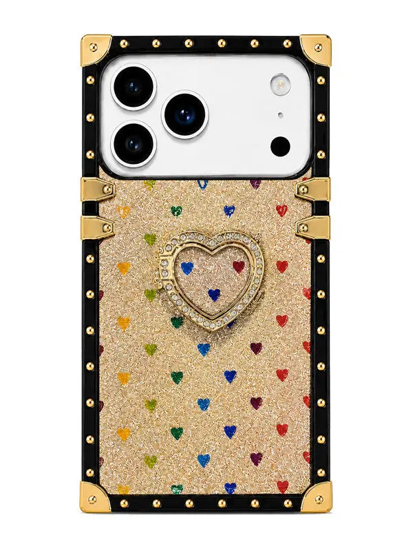 A protective phone case with a luxury trunk design, featuring a gold glitter body decorated with small multicolored hearts, a central rhinestone-embellished heart stand, and a black border with gold-tone studs and corner protectors.