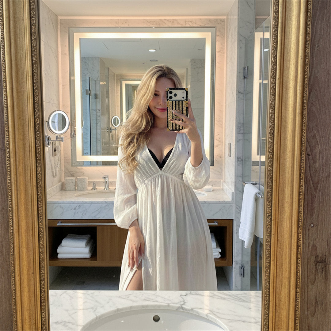Woman taking a mirror selfie in a bathroom wearing a white dress.