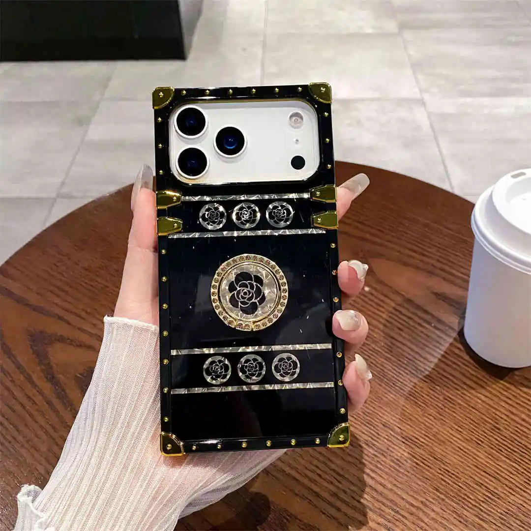Black ornate iPhone 17 Pro case held by a hand on a wooden table.