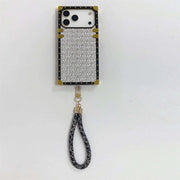 A luxury-style phone case with a textured silver and black chevron pattern, gold corner accents, and a matching black-and-silver wrist strap, shown on a plain white background.