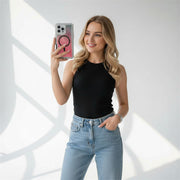 Woman taking a selfie with a phone, wearing a black sleeveless top and blue jeans, on a white background.