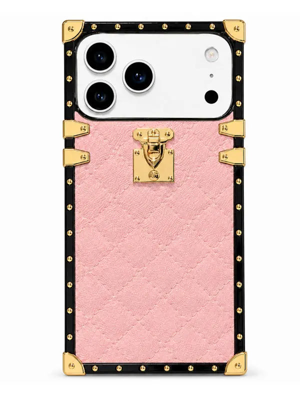 A pink textured phone case designed to look like a luxury trunk, featuring a black border with gold-tone studs, corner protectors, and a central gold clasp lock, shown on a white smartphone.