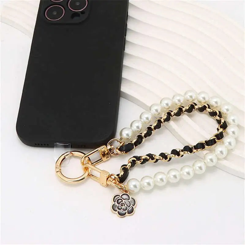 Pearl and gold chain phone strap with black flower charm on a white surface.
