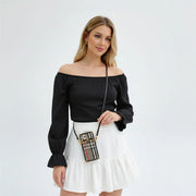 Woman wearing a black off-shoulder top and white skirt with a plaid handbag on a light gray background