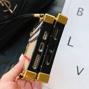 Close-up of a black and gold phone case with a patterned interior, held by a hand against a blurred background.