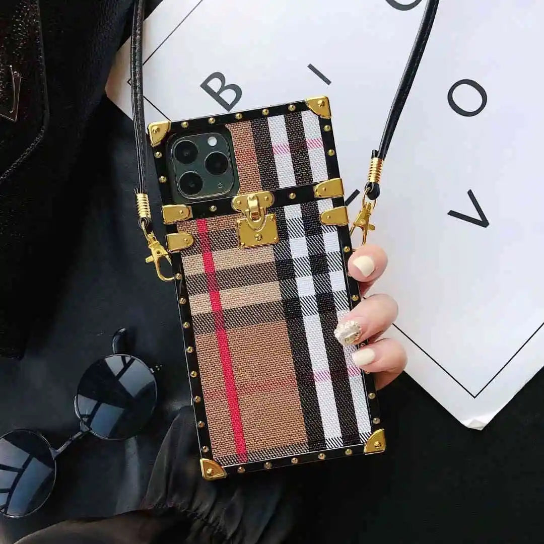 square Phone case with plaid design and gold accents held by a hand, with sunglasses and a white card in the background.