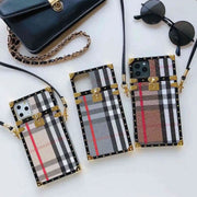 Plaid patterned phone cases with gold accents on a white surface, with a handbag and sunglasses in the background.