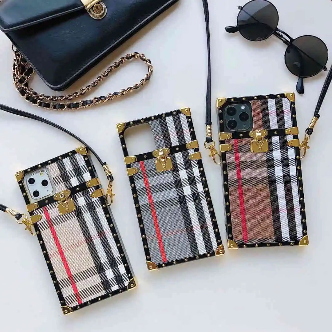 Plaid patterned phone cases with gold accents on a white surface, with a handbag and sunglasses in the background.