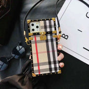 Trunk Phone case with plaid design and gold accents held by a hand on a dark surface.