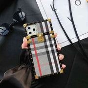 Trunk Phone case with plaid pattern held by a hand on a dark surface with sunglasses and a white paper in the background.