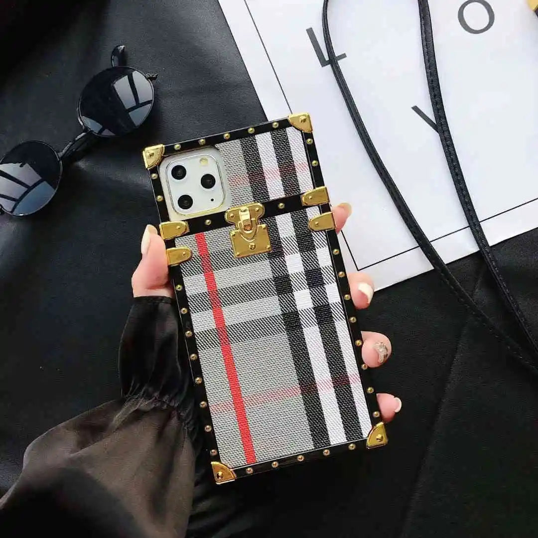 Trunk Phone case with plaid pattern held by a hand on a dark surface with sunglasses and a white paper in the background.