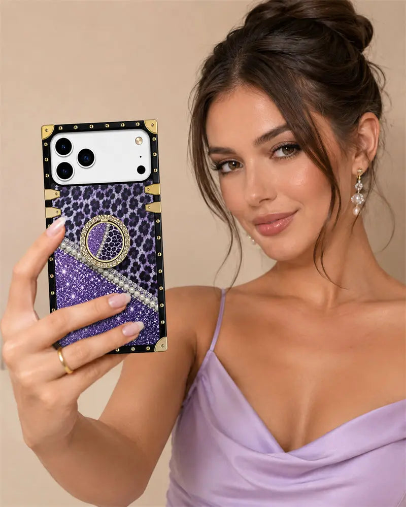 A woman takes a mirror selfie showing off a custom phone case. The case features a purple leopard print top section, a purple glitter lower section, a white rhinestone-embellished diagonal stripe, and black trim with gold studs and corner accents.