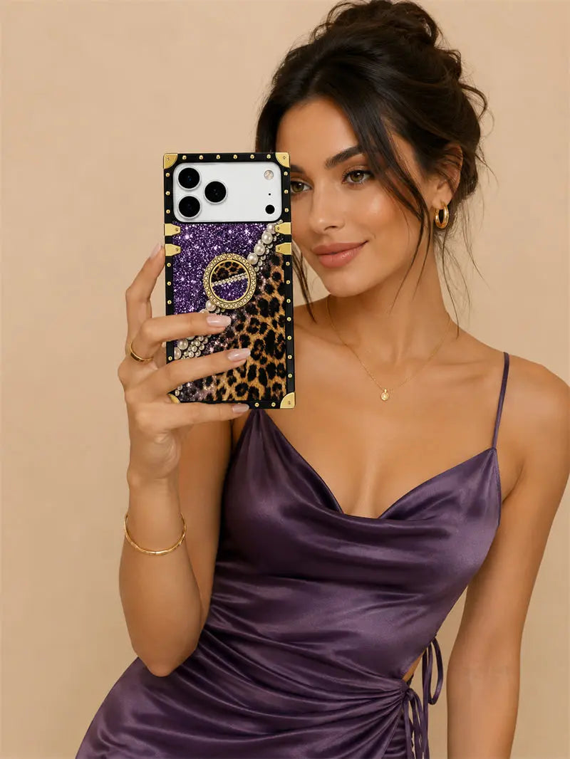 A woman in a purple satin dress takes a mirror selfie showing a phone case with a purple glitter and leopard print design, gold studs, and a gold ring stand.