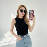 Woman taking a mirror selfie wearing sunglasses and a black sleeveless top with light blue jeans.
