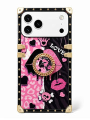 A protective phone case with a luxury trunk design, featuring a split pink and black graphic pattern with gold-tone studs, corner protectors, and a lip-shaped pop socket.