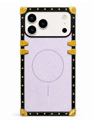 A protective phone case with a black border, gold corner protectors and rivets, and a light purple textured center panel featuring a faint MagSafe ring.