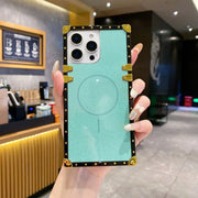 A hand holding a light blue magnetic phone case with a black and gold faux-leather border, shown in a cafe setting.