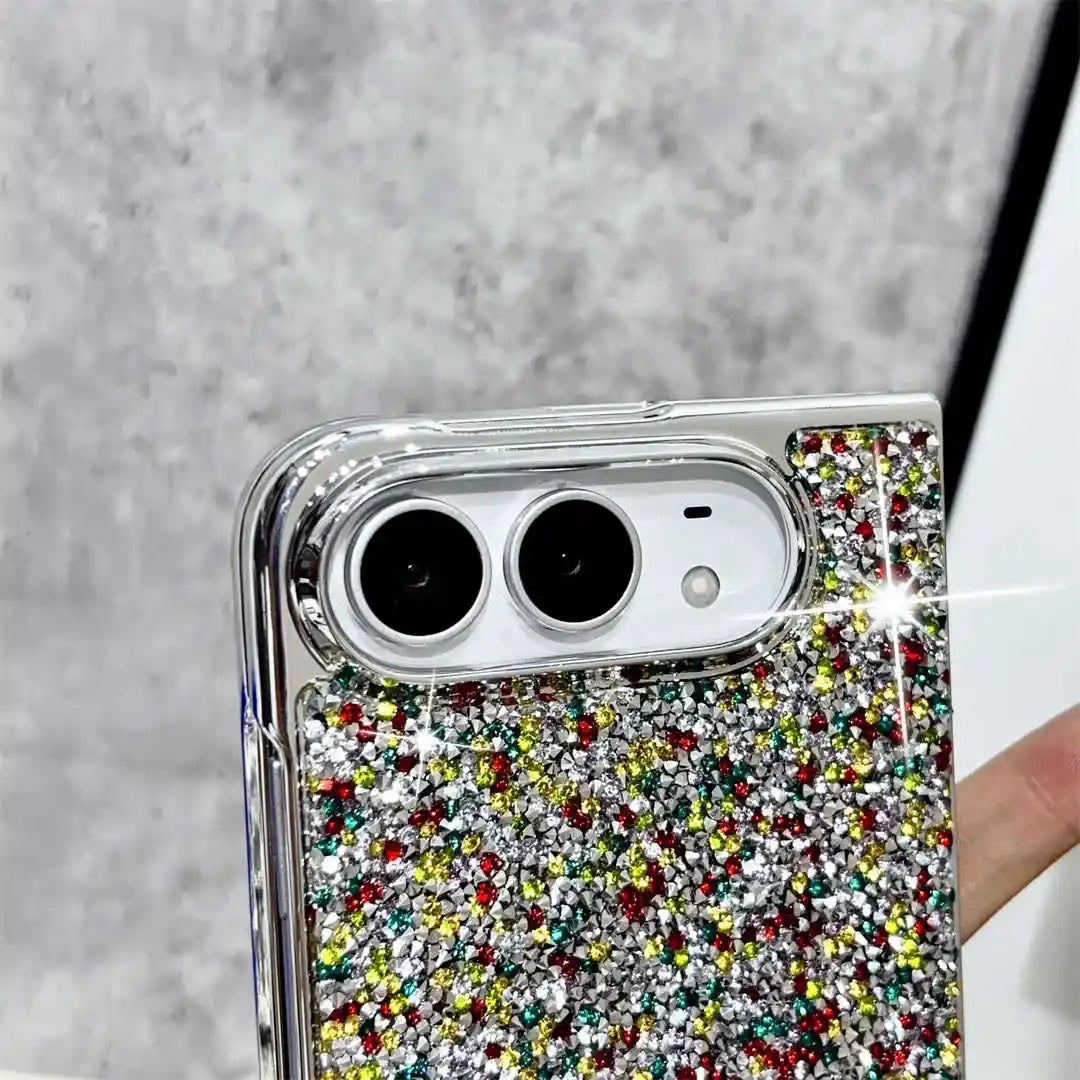 A close-up of a smartphone case covered in dense multicolor rhinestones and glitter, with a clear bumper edge and camera cutout, held against a gray textured background.