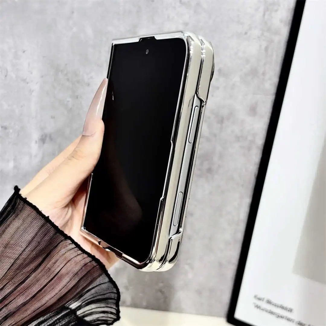 A hand with long nude manicured nails holds an iPhone Duo in a slim, metallic silver case with a black screen. The background is a textured gray wall with a framed print partially visible on the right.