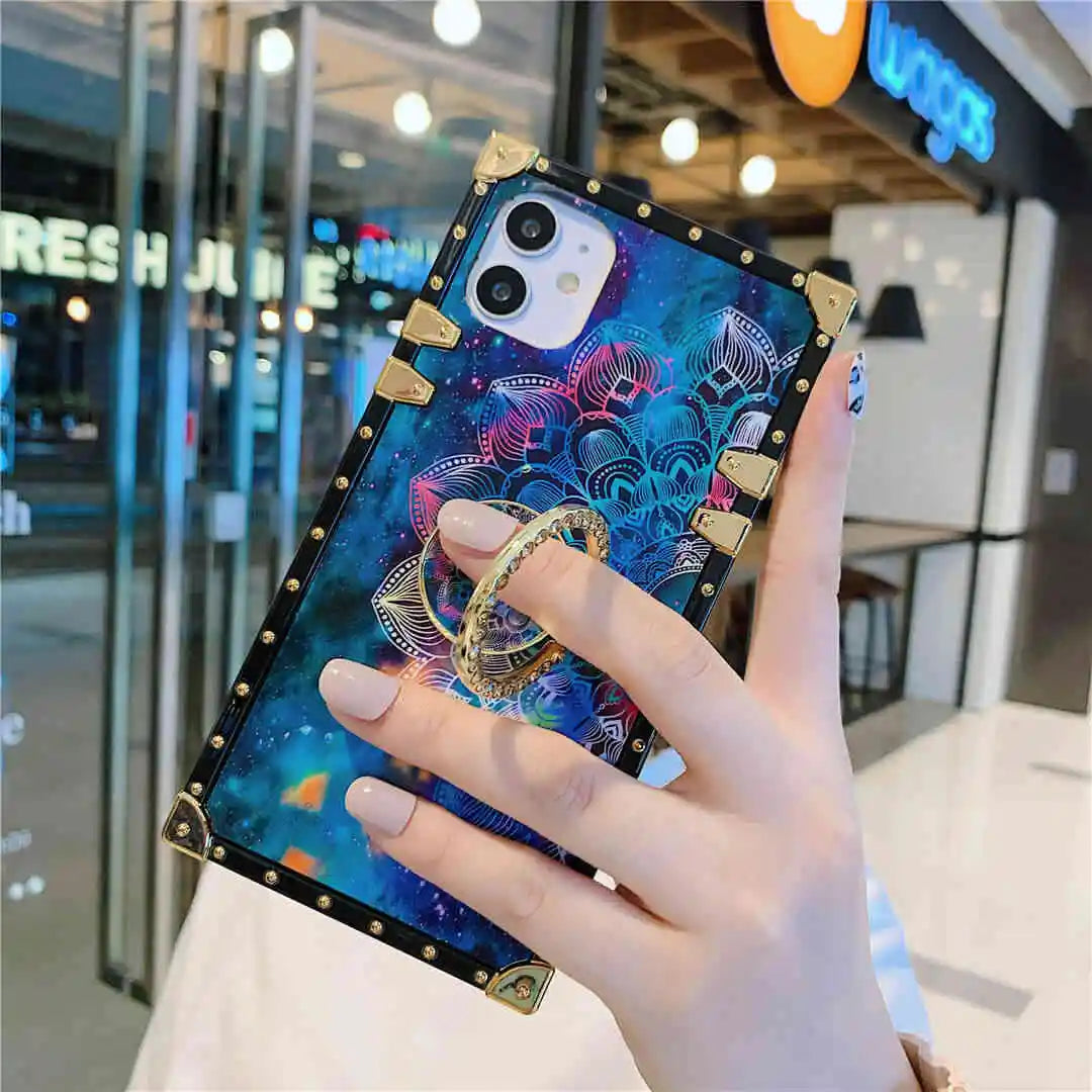 Phone case with mandala design and ring holder held by a hand in an indoor setting.