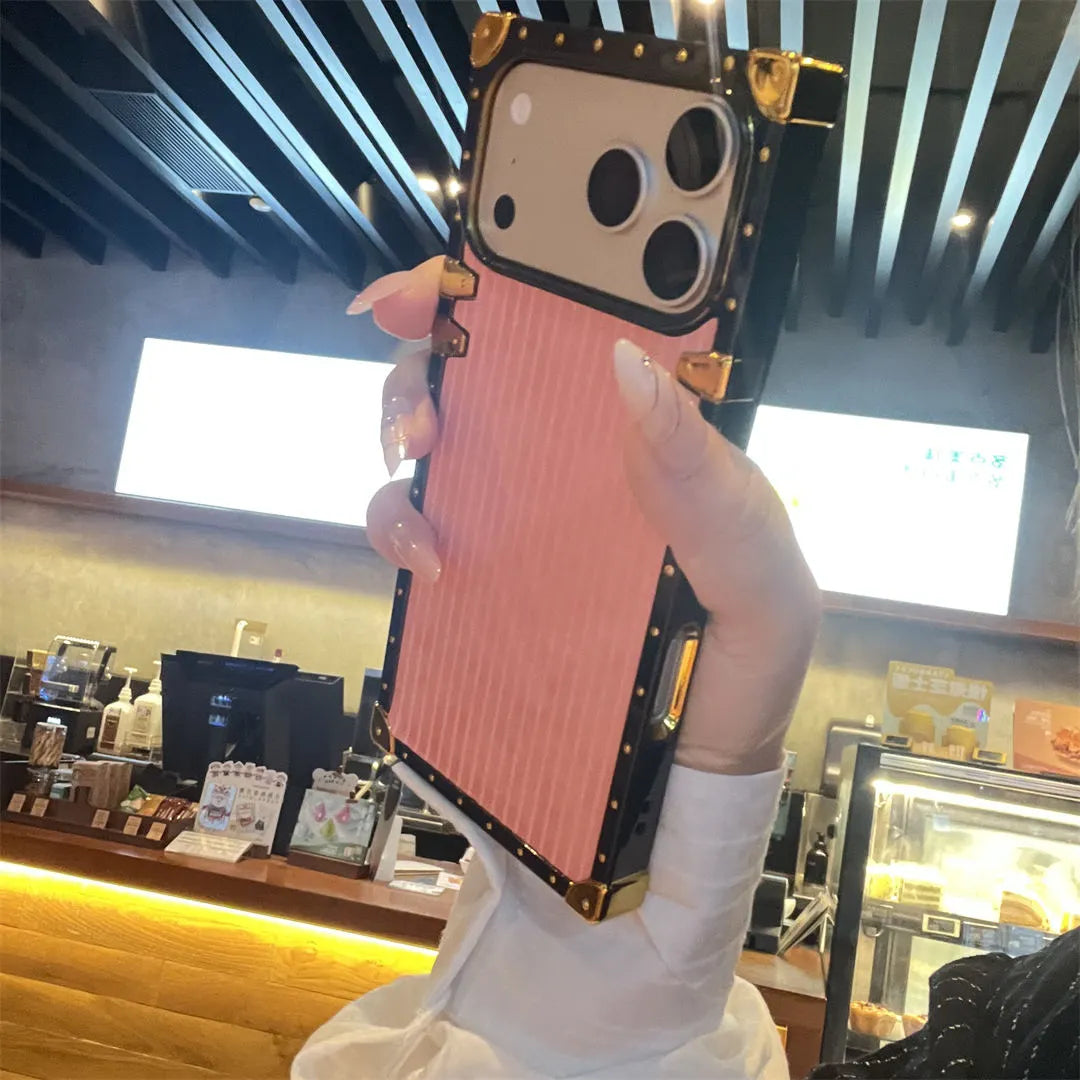 Phone case with pink and gold design held by a hand in a cafe setting