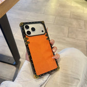 Person holding a phone with an orange case on a tiled floor.