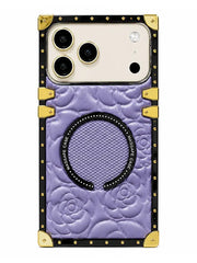 A luxury phone case featuring a lavender purple embossed floral pattern, a black studded circular magnetic ring, and gold-tone metal corner protectors and accents, shown on a white background.
