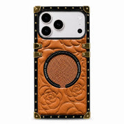 A protective phone case with a brown embossed leather-like floral design, a circular magnetic ring, and a black border with gold-tone rivets and corner protectors, shown on a light gray background.