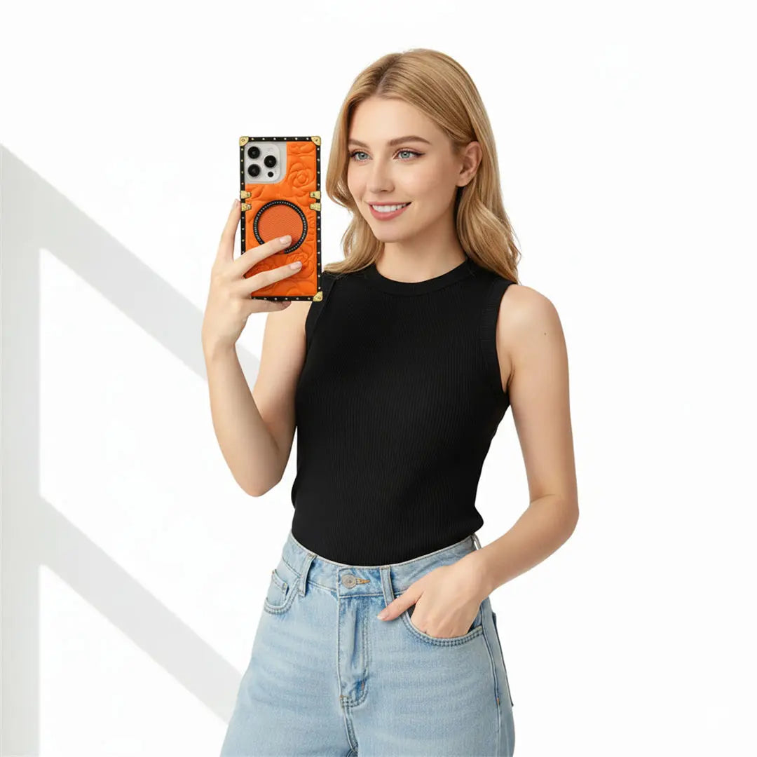 A woman holding a smartphone with an orange and black patterned case, wearing a black sleeveless top and light blue jeans against a white background.