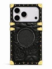 A black embossed leather phone case with gold-tone metal corner protectors and rivets, featuring a circular speaker grille and a large camera cutout, shown on a white background.